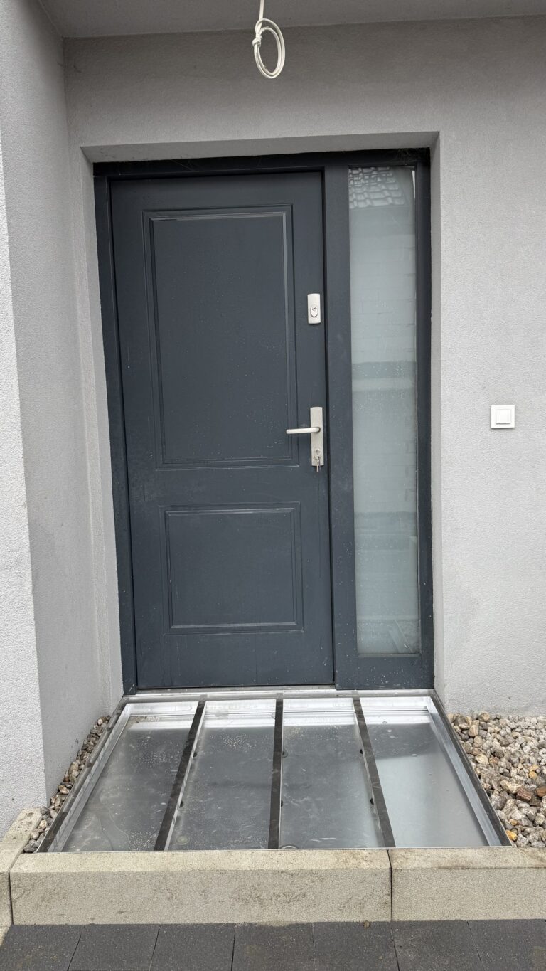 Osadnik aluminiowy we wnęce przed drzwiami domu