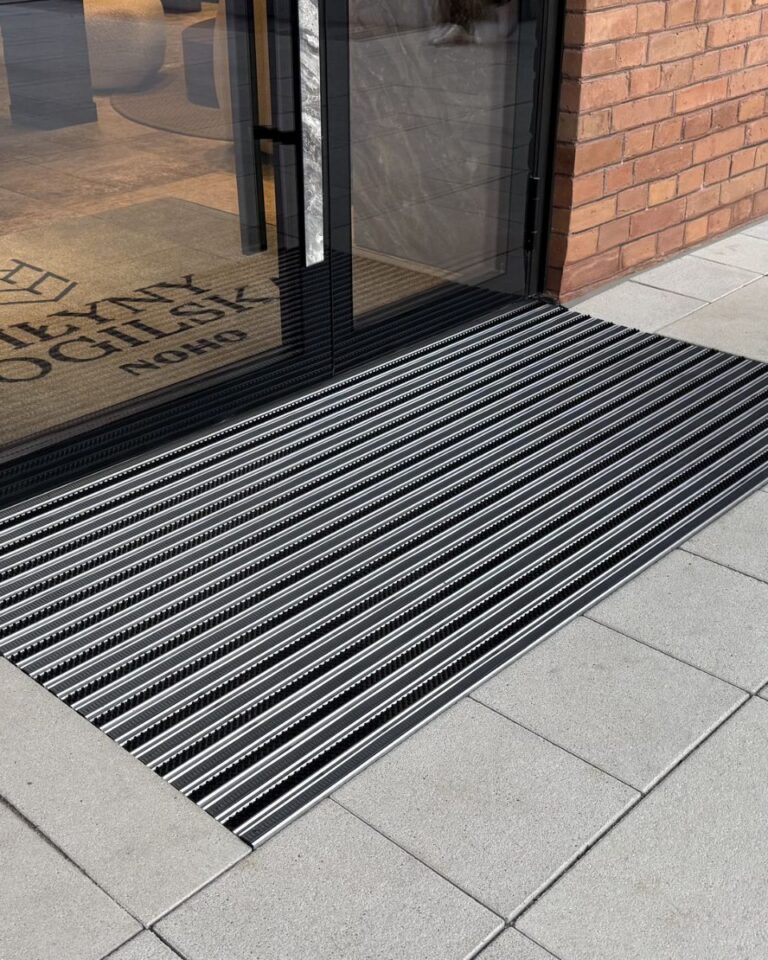 Wycieraczka aluminiowa NEVRA przed szklanymi drzwiami wejścia w ceglanej elewacji, Młyny Mogilska, Kraków